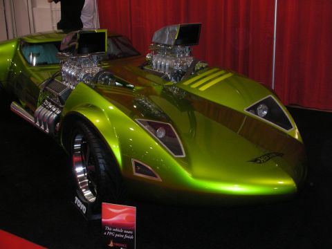 1998 Ford Crown Victoria - green twin-engine custom car bearing a Hot Wheels flame logo sits on a black stand in front of a red curtain.