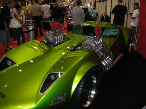 1998 Ford Crown Victoria - green custom car showing two exposed blown engines and a teal interior is surrounded by spectators at an indoor show.