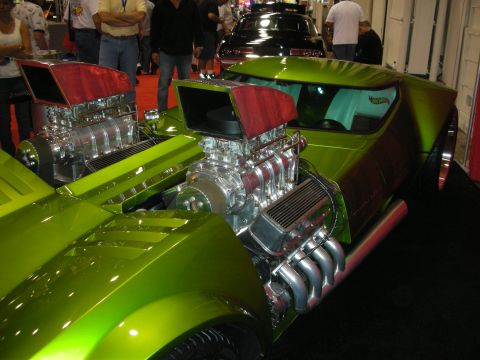 1998 Ford Crown Victoria - Two green custom cars with raised hoods and exposed supercharged engines are parked side by side on a show floor.