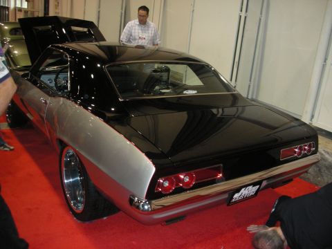 1998 Ford Crown Victoria - rear three-quarter of a black-and-silver custom muscle coupe with round taillights sits on red carpet as a man looks on.