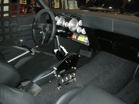 1998 Ford Crown Victoria - black custom car interior shows a small racing steering wheel, a cluster of round gauges and an exposed shifter assembly.