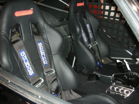 1998 Ford Crown Victoria - Two black bucket seats fitted with blue Sparco harnesses sit beside a roll cage and shifter inside a custom car.