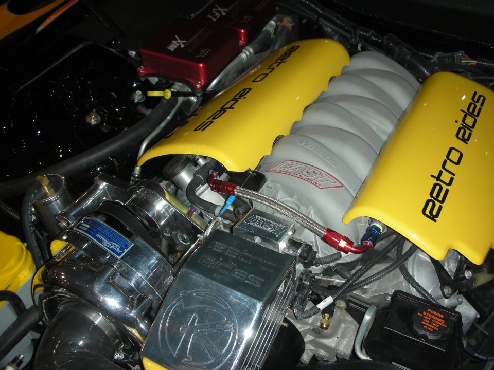 Photo of a yellow-and-chrome LS-style engine bay with Retro Aides valve covers and a supercharger