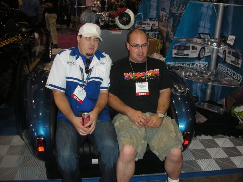1998 Ford Crown Victoria - Two men sit on a custom car-rear-shaped bench in front of a Shelby vendor booth at an indoor show.