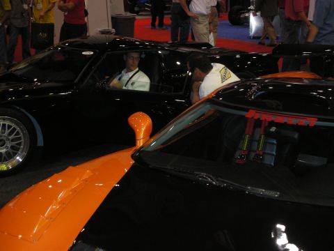 1998 Ford Crown Victoria - orange supercar and a black supercar with red racing harnesses are parked together on a carpeted show floor.