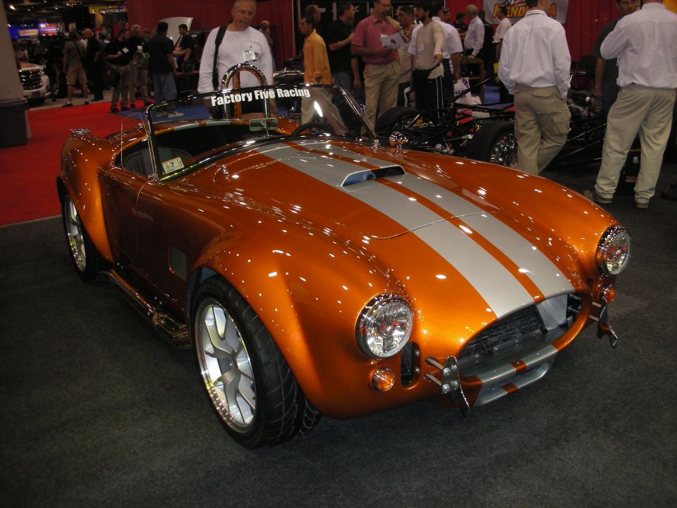 Copper-orange Cobra roadster with silver stripes at Factory Five Racing booth