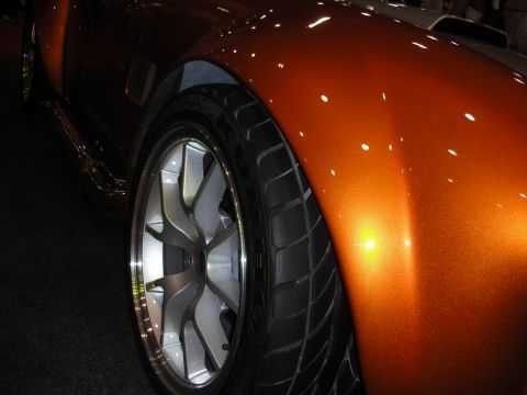 1998 Ford Crown Victoria - Close-up of a copper metallic fender and a polished multi-spoke wheel with low-profile tire on a roadster.