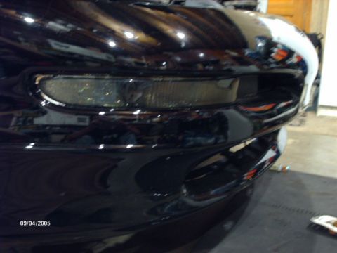 1995 Ford Probe - Close-up of a black car's front bumper and headlight assembly, showing reflective surfaces.