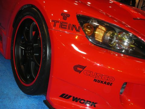 1998 Ford Crown Victoria - Close-up of a red Honda S2000 front fender and projector headlight with Tein, Cusco Nukabe, and Work decals on black wheels.