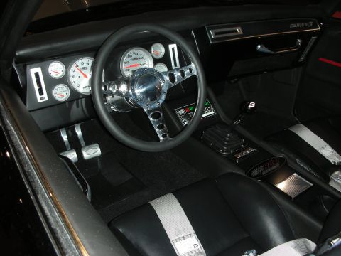 1998 Ford Crown Victoria - Black custom car interior showing white-faced Auto Meter gauges, a chrome-spoke steering wheel, drilled pedals, and a Series 3 badge.