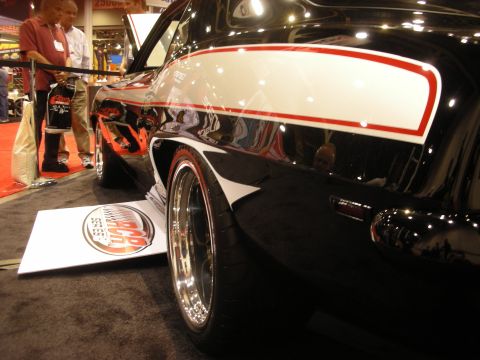 1998 Ford Crown Victoria - Low-angle view of a black show car's flank showing a white panel with red pinstripe above a deep-dish chrome wheel on a dark carpeted floor.