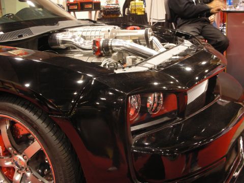 1998 Ford Crown Victoria - Detail of a black custom car's open engine bay with a polished twin-screw supercharger and chrome intake tubes above red-accented headlight…