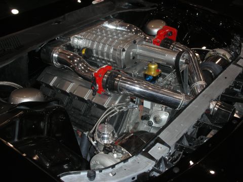 1998 Ford Crown Victoria - Close-up of a polished Roots-type supercharger and chrome intake tubing mounted on a V8 in a black-painted engine compartment.