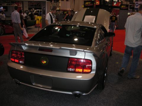 1998 Ford Crown Victoria - Rear view of a silver late-model Ford Mustang coupe with a rear spoiler and twin exhaust tips on display among booths.