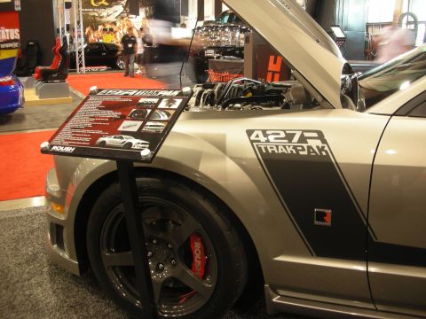 1998 Ford Crown Victoria - Front quarter of a silver Roush Mustang with '427R Trak Pak' side graphics, hood raised and red Roush brake calipers behind a spec placard.