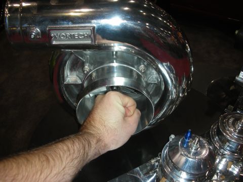 1998 Ford Crown Victoria - Close-up of a person's hand resting on a polished Vortech centrifugal supercharger with smaller polished components alongside.