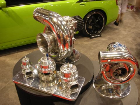 1998 Ford Crown Victoria - Two large polished turbochargers and chrome wastegates arranged on a display table with a green tuner car in the background.