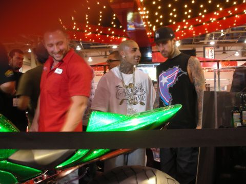 1998 Ford Crown Victoria - Several men, some tattooed and wearing chains, stand and smile around a green custom motorcycle in a lively show area with string lights.