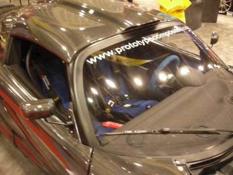 1998 Ford Crown Victoria - Front view through the windshield of a carbon-fiber roadster bearing a 'www.prototypecomposites.com' banner over blue racing seats.