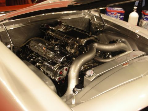 1998 Ford Crown Victoria - polished overhead-cam V engine sits in the smoothed silver engine bay of a custom car, with chrome plumbing and NX nitrous bottles behind.