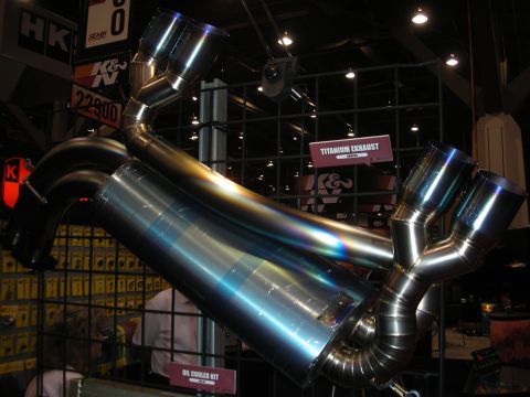 1998 Ford Crown Victoria - polished titanium exhaust system with merged Y-pipes and quad burnt-blue tips shown at a K&N 'Titanium Exhaust' booth display.