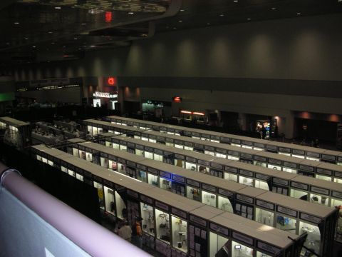 1998 Ford Crown Victoria - Aerial view inside a dimly lit convention center showing long rows of small curtained trade-show booths.