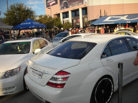 1998 Ford Crown Victoria - White Mercedes-Benz S-Class sedan on black wheels parked beside another white sedan at an outdoor car event.