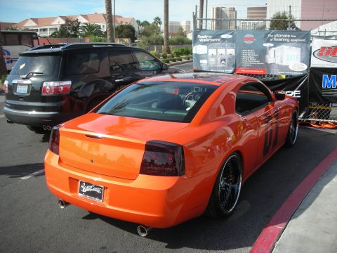 1998 Ford Crown Victoria - Orange Dodge Charger sedan with smoked taillights and custom wheels parked outdoors beside a black SUV.