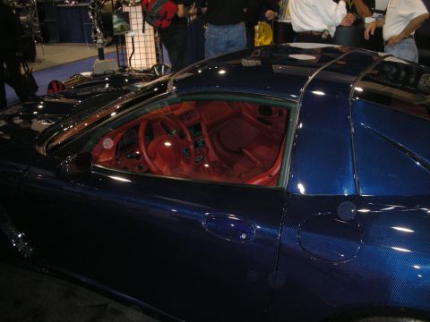 1998 Ford Crown Victoria - Side view of a dark blue carbon-fiber-bodied sports car with a bright red interior at an indoor exhibition.