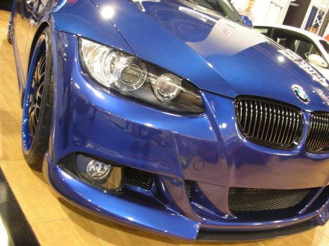 1998 Ford Crown Victoria - Blue BMW 3 Series coupe front three-quarter with halo headlights and aftermarket body kit on a show floor.