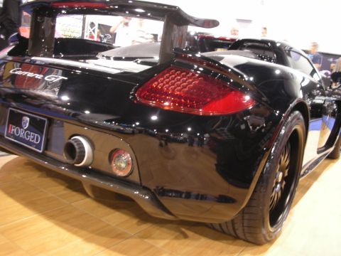 1998 Ford Crown Victoria - Rear view of a black Porsche Carrera GT supercar with an iForged plate displayed on an indoor show floor.