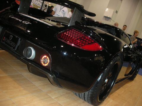 1998 Ford Crown Victoria - Rear quarter view of a black Porsche Carrera GT on black wheels with an iForged plate at an indoor show.