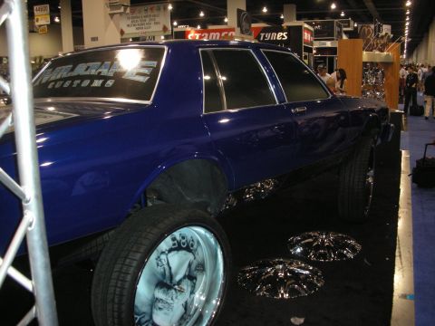1998 Ford Crown Victoria - Blue boxy Chevrolet Caprice sedan on tall custom wheels with extra chrome rims laid out on the floor.