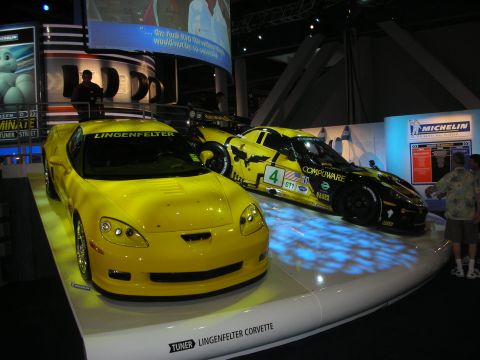 1998 Ford Crown Victoria - Yellow Lingenfelter Corvette displayed next to a black Compuware race Corvette on a lit show platform.