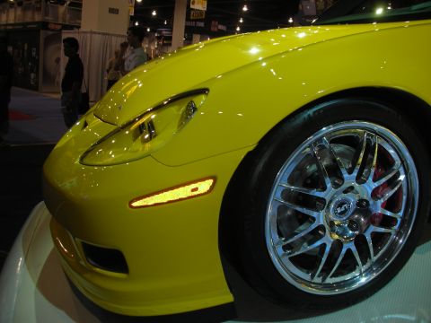 1998 Ford Crown Victoria - yellow front fender, headlight and polished chrome wheel of a Corvette photographed at an indoor automotive show.