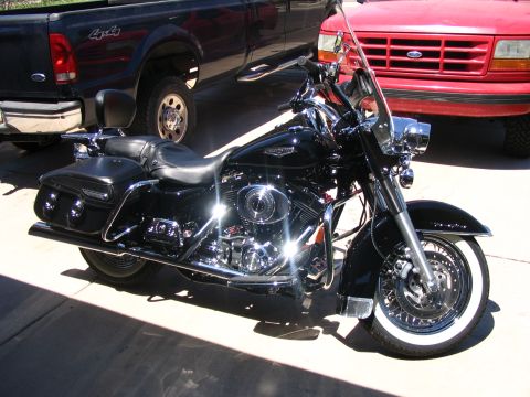 2006 Harley-Davidson FLH - A black 2006 Harley-Davidson FLH motorcycle is parked outdoors next to two trucks.