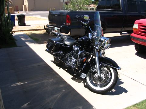 2006 Harley-Davidson FLH - A black motorcycle is parked next to a black pickup truck and a red vehicle.
