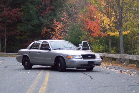 2001 Ford Crown Victoria - A silver 2001 Ford Crown Victoria sedan is parked on a road with its driver's door ajar, set against a backdrop of colorful autumn foliage.