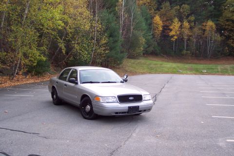 2001 Ford Crown Victoria - A silver 2001 Ford Crown Victoria is parked in an asphalt lot with trees and grass in the background.