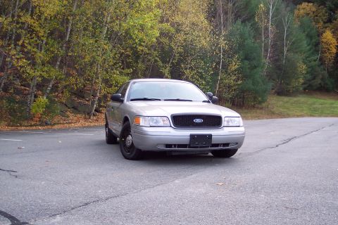 2001 Ford Crown Victoria - A silver 2001 Ford Crown Victoria is parked on an asphalt surface with autumn foliage visible in the background.