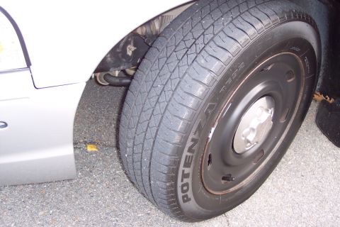 2001 Ford Crown Victoria - Close-up of a white car's fender and tire, showing the 'POTENZA' tire branding.