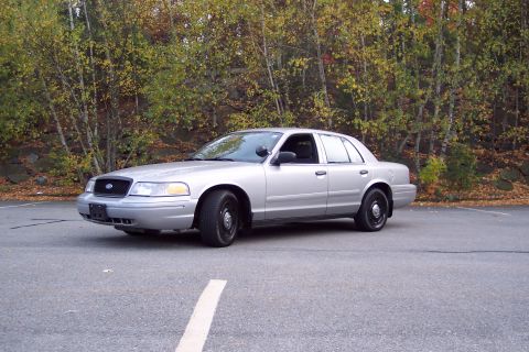 2001 Ford Crown Victoria - A silver 2001 Ford Crown Victoria is parked in an asphalt lot with fall foliage behind it.