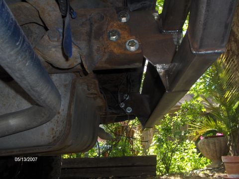 1986 Ford Bronco - Close-up of a vehicle's undercarriage, revealing custom metalwork and a rusty exhaust system.