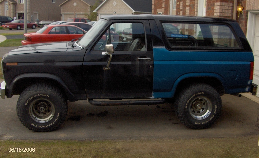 Side view of a black and blue Ford Bronco with aftermarket wheels and tires. The front fender is black, and the rear quarter panel is blue