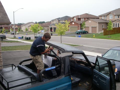 1986 Ford Bronco - Two men work on the interior of a teal Ford Bronco with its top removed, parked in a suburban driveway.