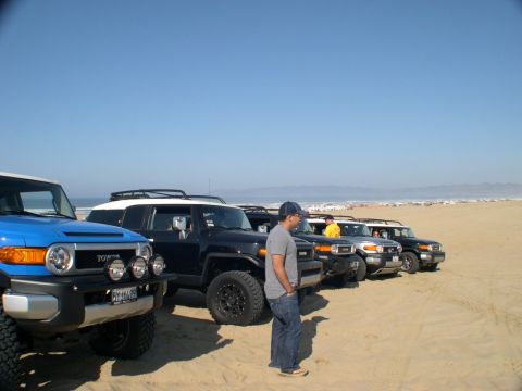 2007 Toyota FJ Cruiser - A line of Toyota FJ Cruisers are parked on a beach under a clear blue sky.