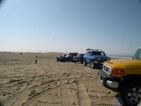 2007 Toyota FJ Cruiser - Several Toyota FJ Cruisers are parked on a sandy terrain near the ocean.