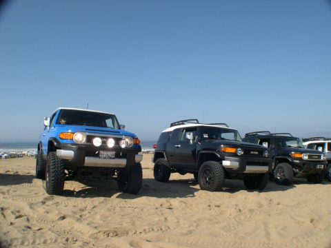 2007 Toyota FJ Cruiser - Several Toyota FJ Cruisers are parked on a sandy beach under a clear blue sky.