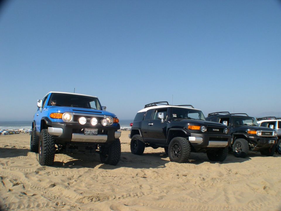 Blue and black lifted Toyota FJ Cruisers lined up on beach sand with driving lights