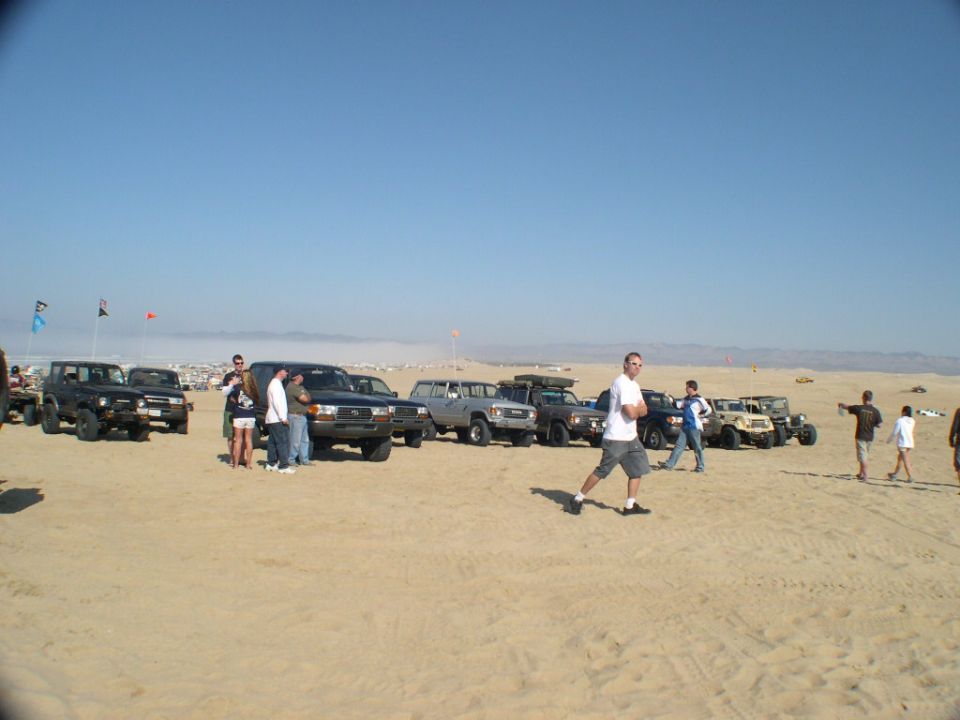 Row of Toyota 4x4 SUVs parked on sand dunes with people gathered around